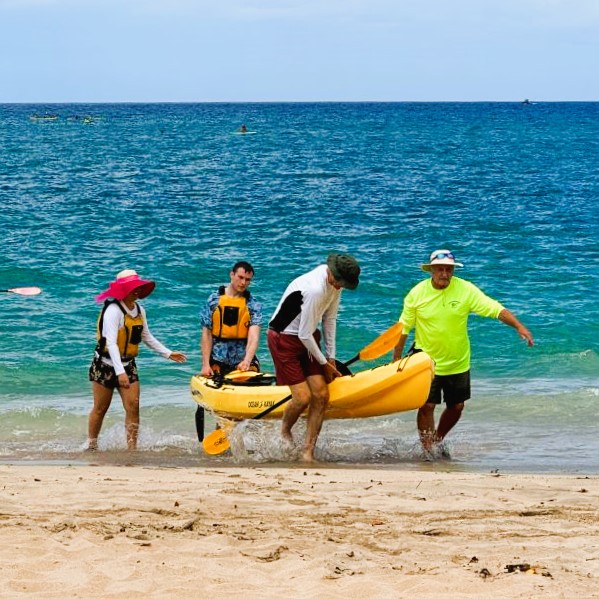 Four people carrying a tandem kayak from the shore