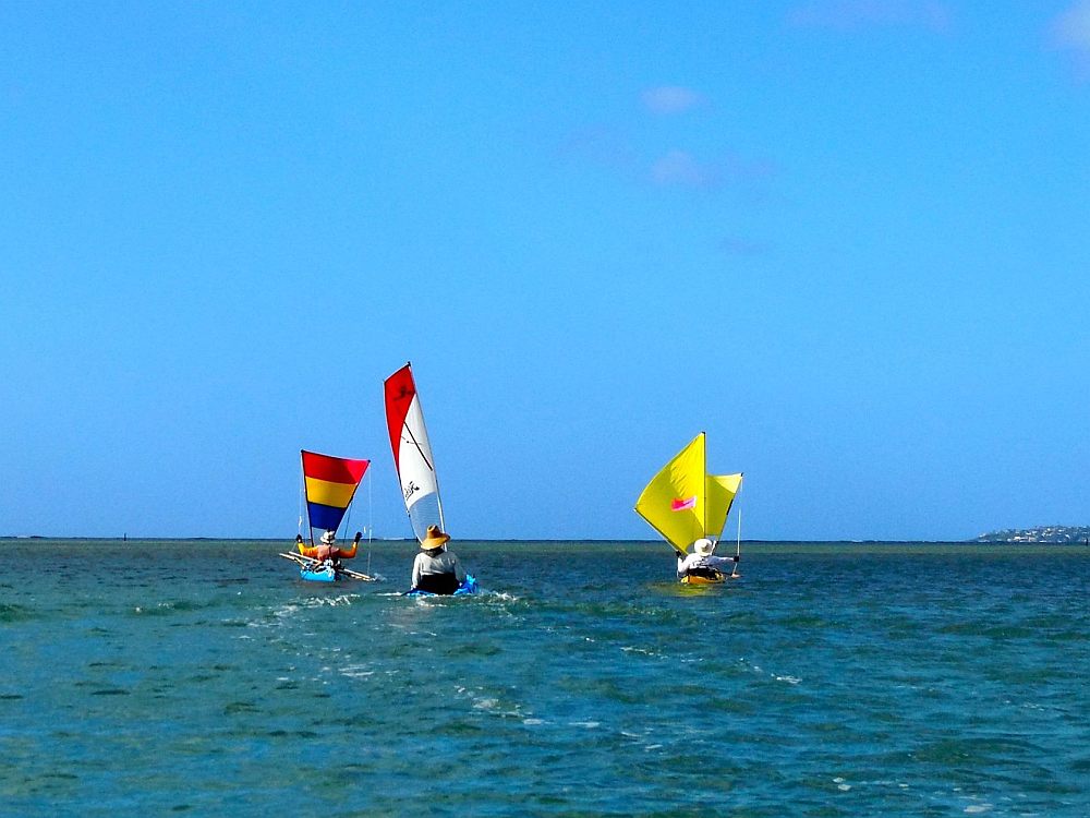 Three kayakers with sails