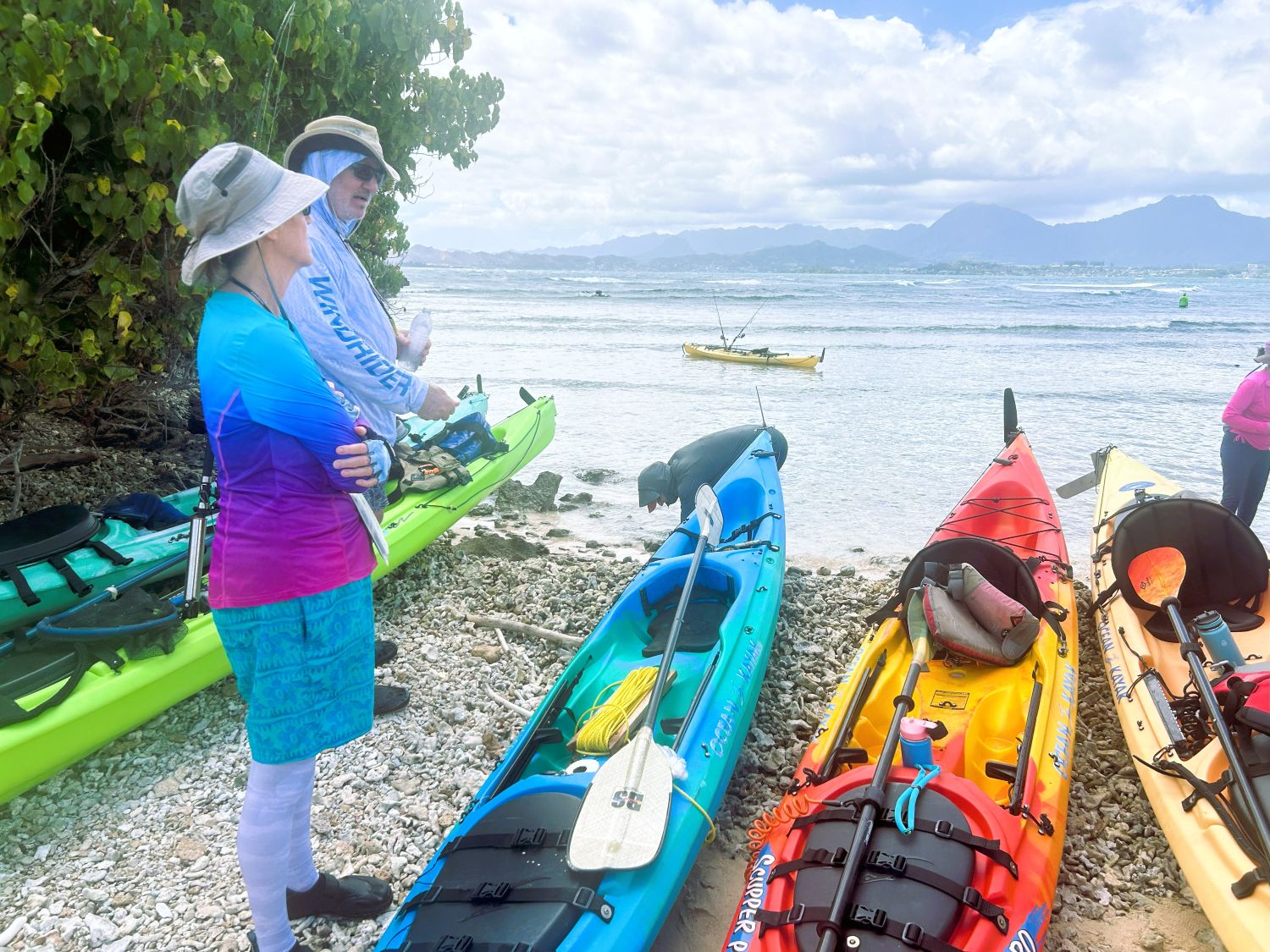 Man and woman standing next to kayaks with Koʻolau range in background